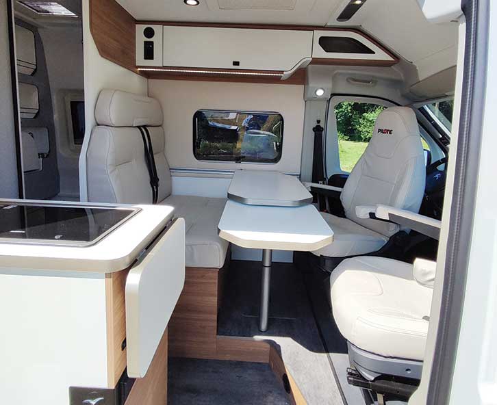 Two cab seats in a motorhome turned around to face a couch seat with a table between them.