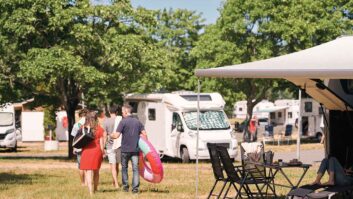 A couple walking along a campsite, with a motorhome in the background